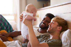 Same Sex Male Couple Holding Up Baby and Smiling  