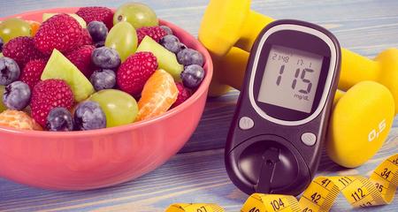 Picture of a healthy bowl of fruit, glucose monitor, weights and a tape measure.