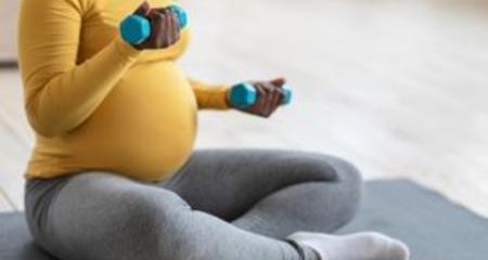 Pregnant woman sitting on a yoga mat holding weights