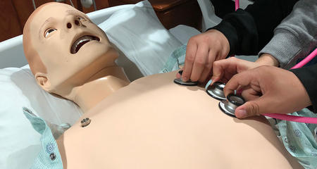 Students listening to the heartbeat of an interactive mannequin.